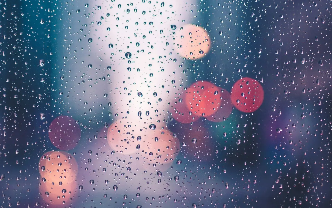 Raindrops on a window with city lights beyond the glass