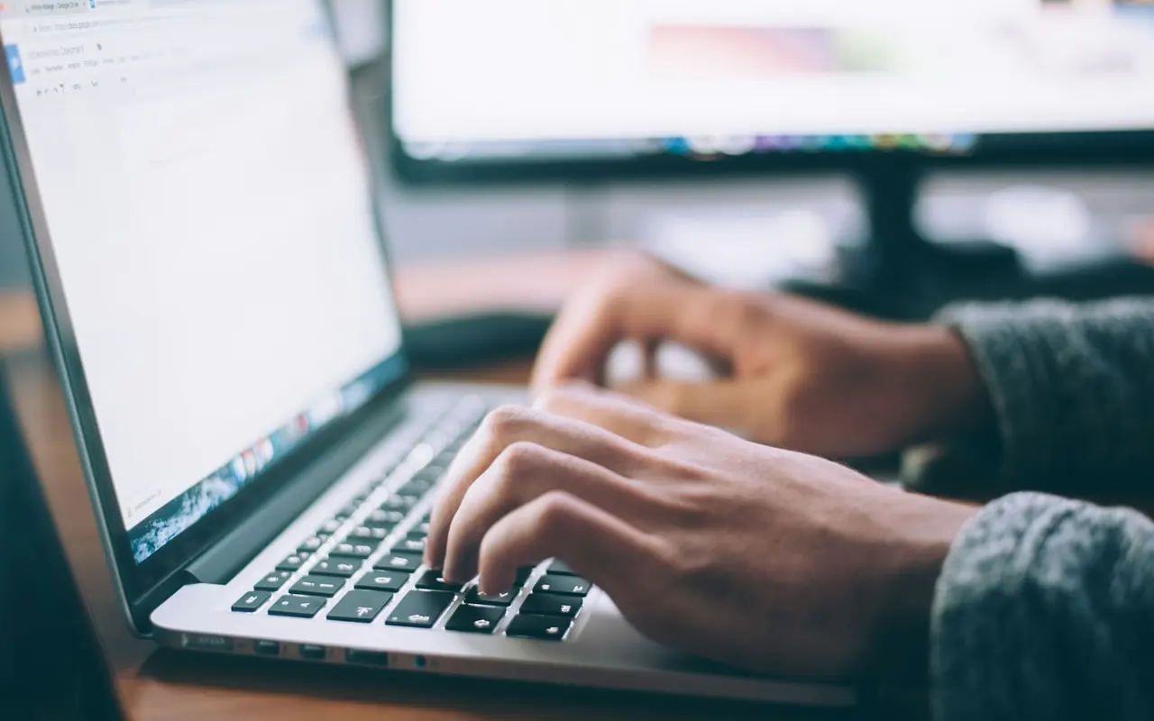 Hands typing on a laptop at a desk